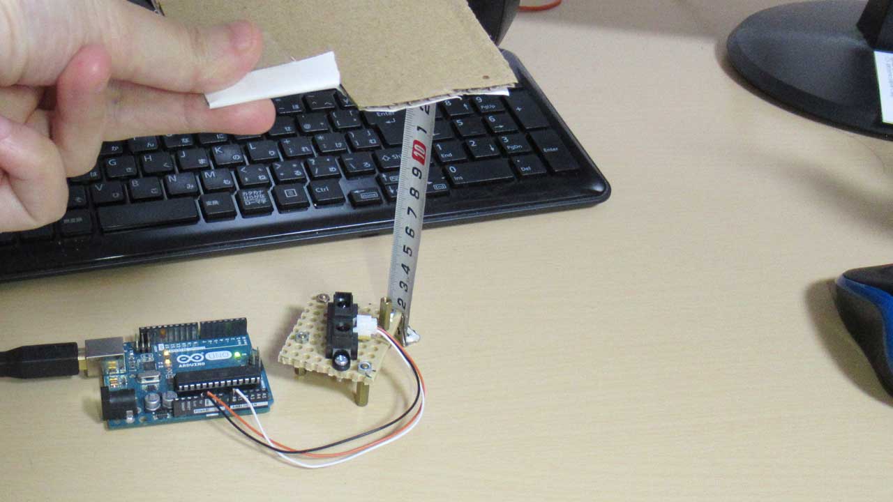 Arduinoに繋いだ測距センサに、紙をかざしている様子